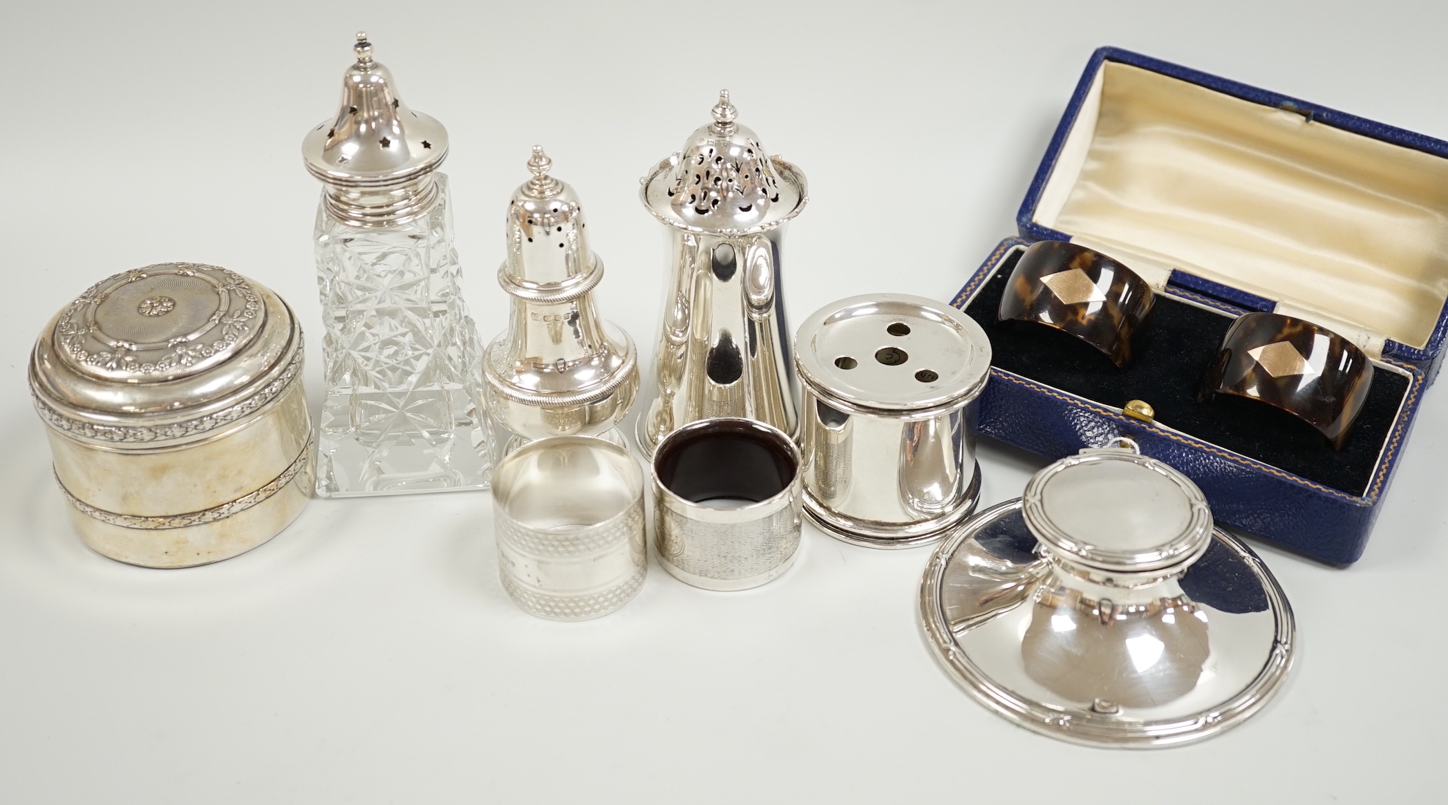 A group of mixed silver including three sugar casters, two inkwells, two pairs of napkin rings (one tortoiseshell) and a white metal box and cover.